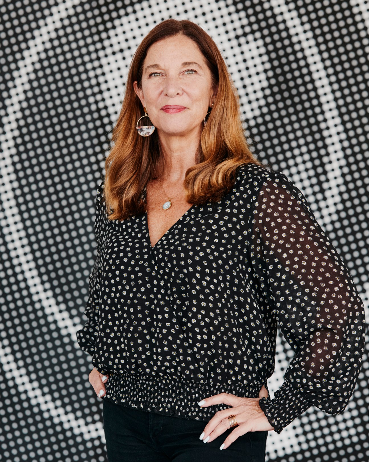 Maria Mingalone in black floral blouse with earrings against geometric patterned background