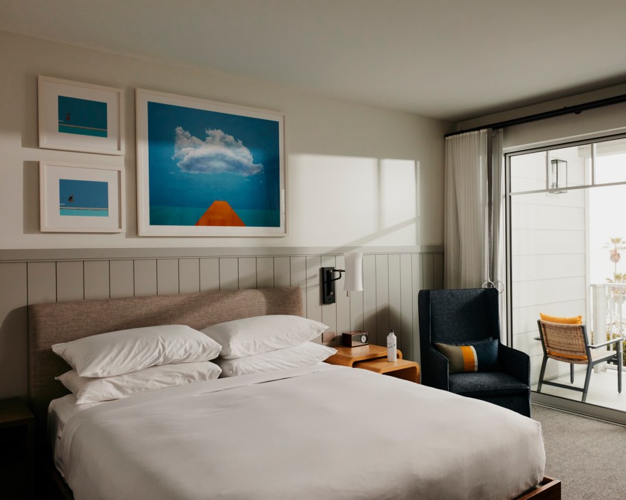 Modern hotel room interior featuring a bed with white linens, contemporary furniture, and large windows providing natural light