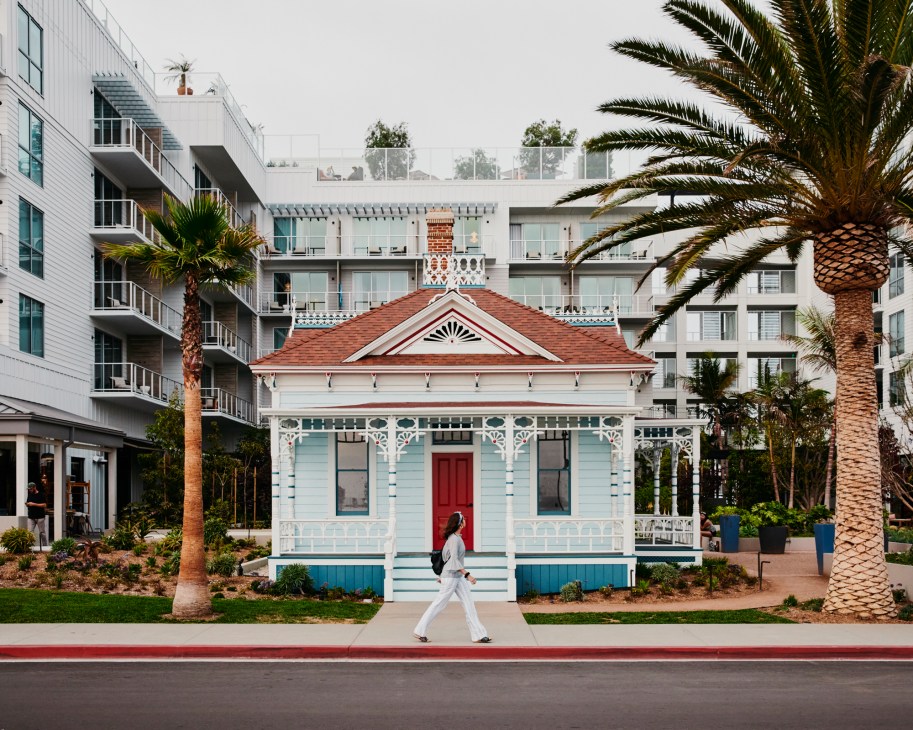 Victorian cottage with turquoise siding, white trim, red door and wraparound porch with person walking past