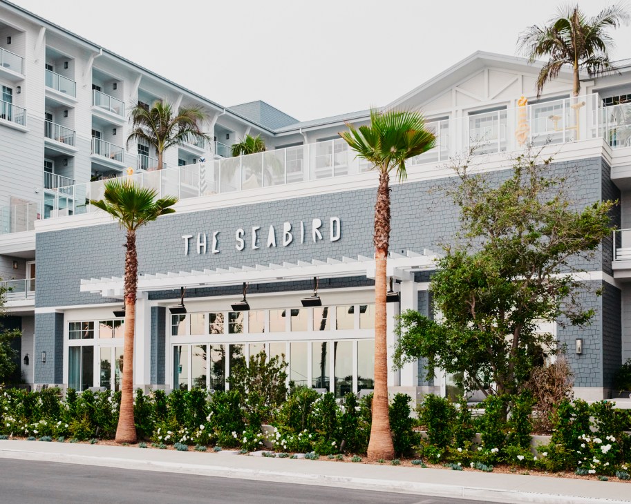 Modern white hotel building with 'THE SEABIRD' signage, featuring contemporary architecture with palm trees and landscaping