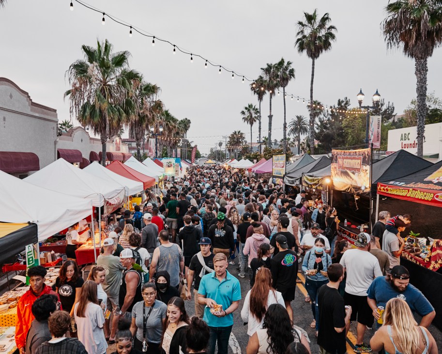 Crowded evening street market with food vendors, colorful tents, and hundreds of people walking between stalls