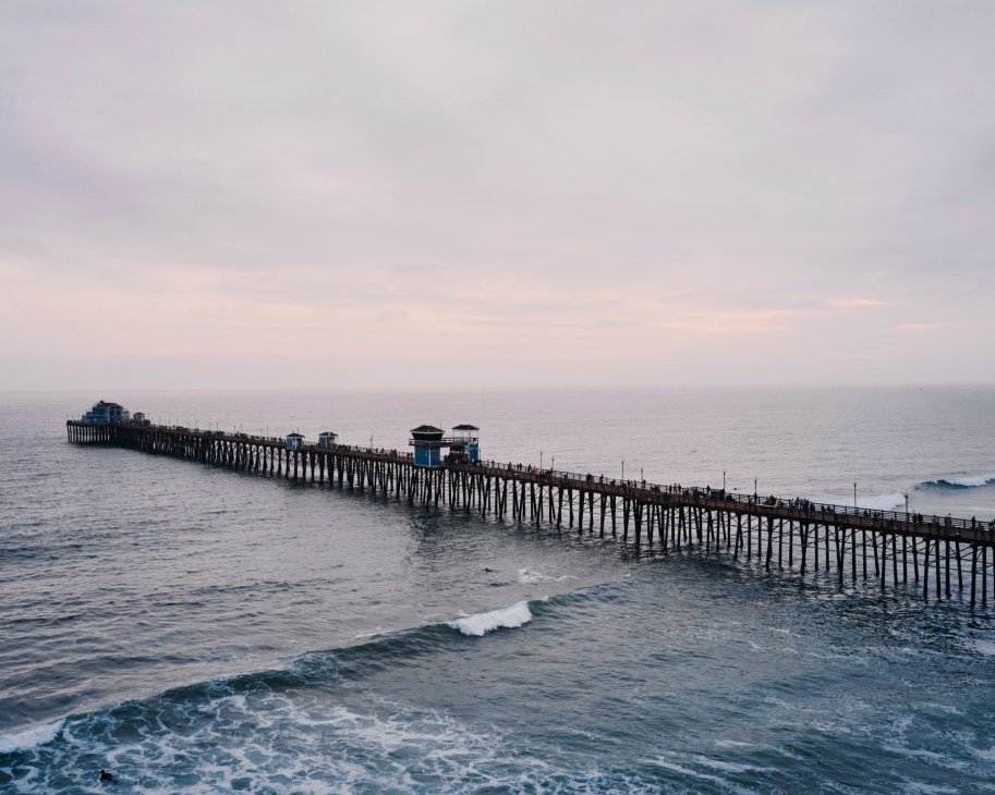 Aerial view of a wooden pier extending into blue ocean waters with waves breaking along the shoreline