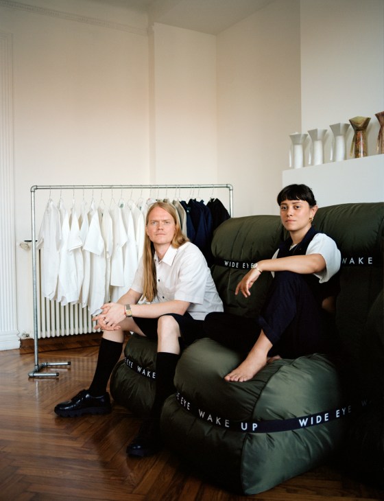 Morten Thuesen and Letizia Caramia sit on their Wide Eye couch in their Milan studio with clothing displayed behind them.