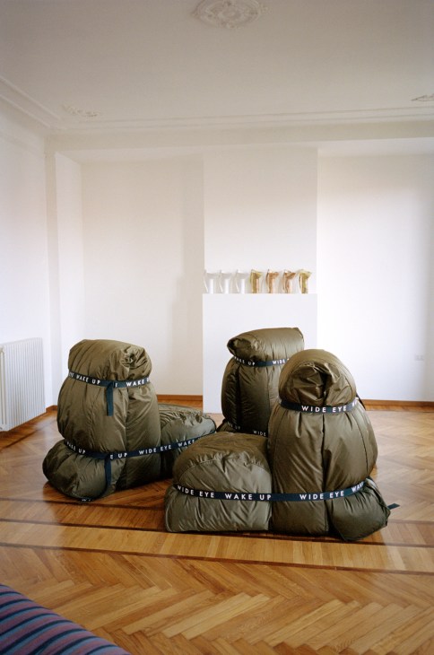Olive-green puffy couch sections with 'Wide Eye Wake Up' text labels arranged in a gallery space with white walls.