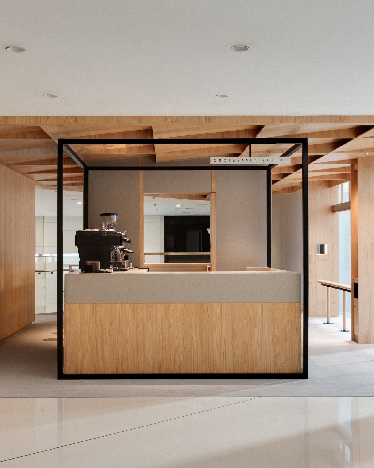 Interior view of Omotesando Koffee Hong Kong showing central coffee bar with black oak and steel frame surrounded by timber elements