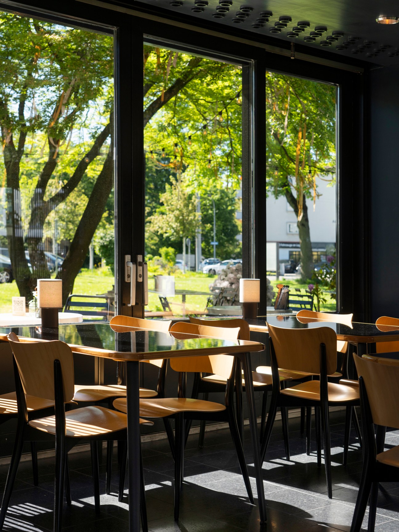 Interior of Ooki Pavilion showing wooden chairs at tables with large windows overlooking green garden.