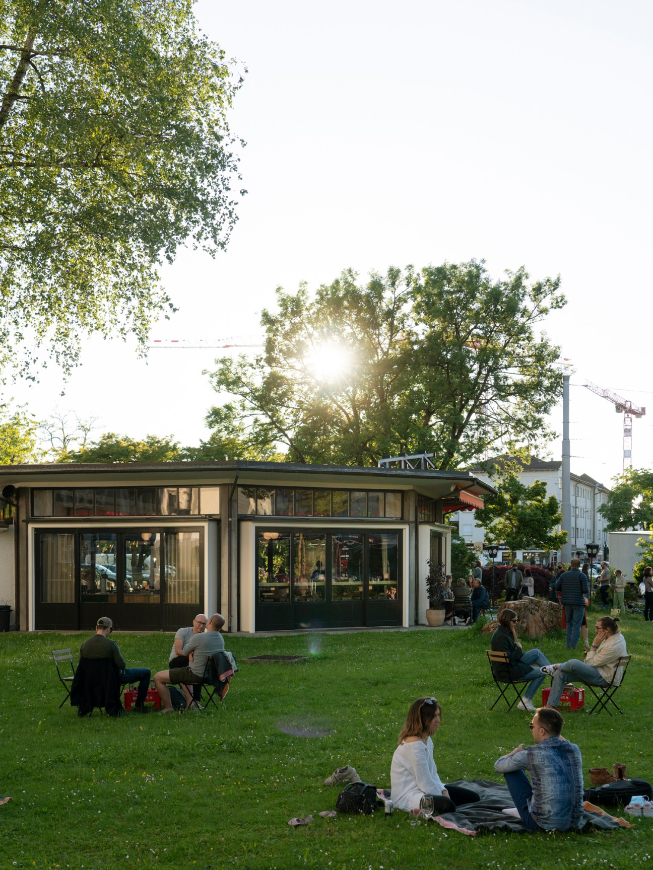 Exterior view of Ooki Pavilion with glass-sided structure surrounded by green lawn and trees, with diners seated outside.