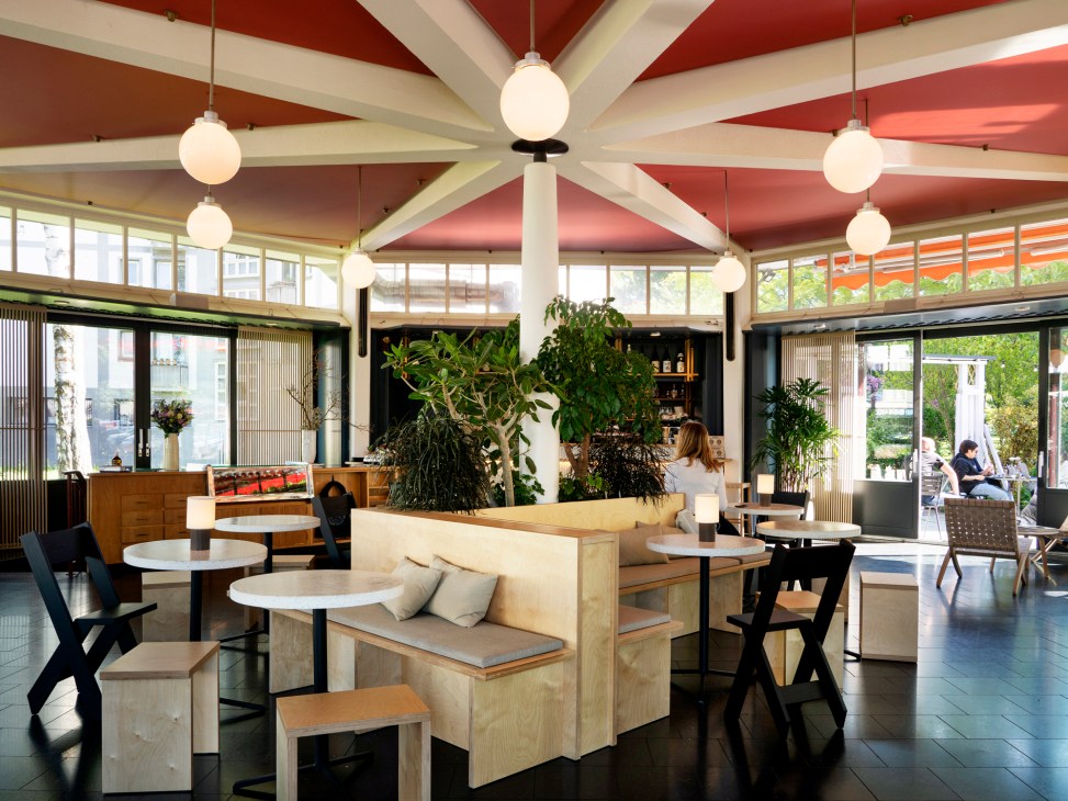 Interior of Ooki Pavilion restaurant showing rust-red ceiling, spherical glass lights, and plywood seating with plants.