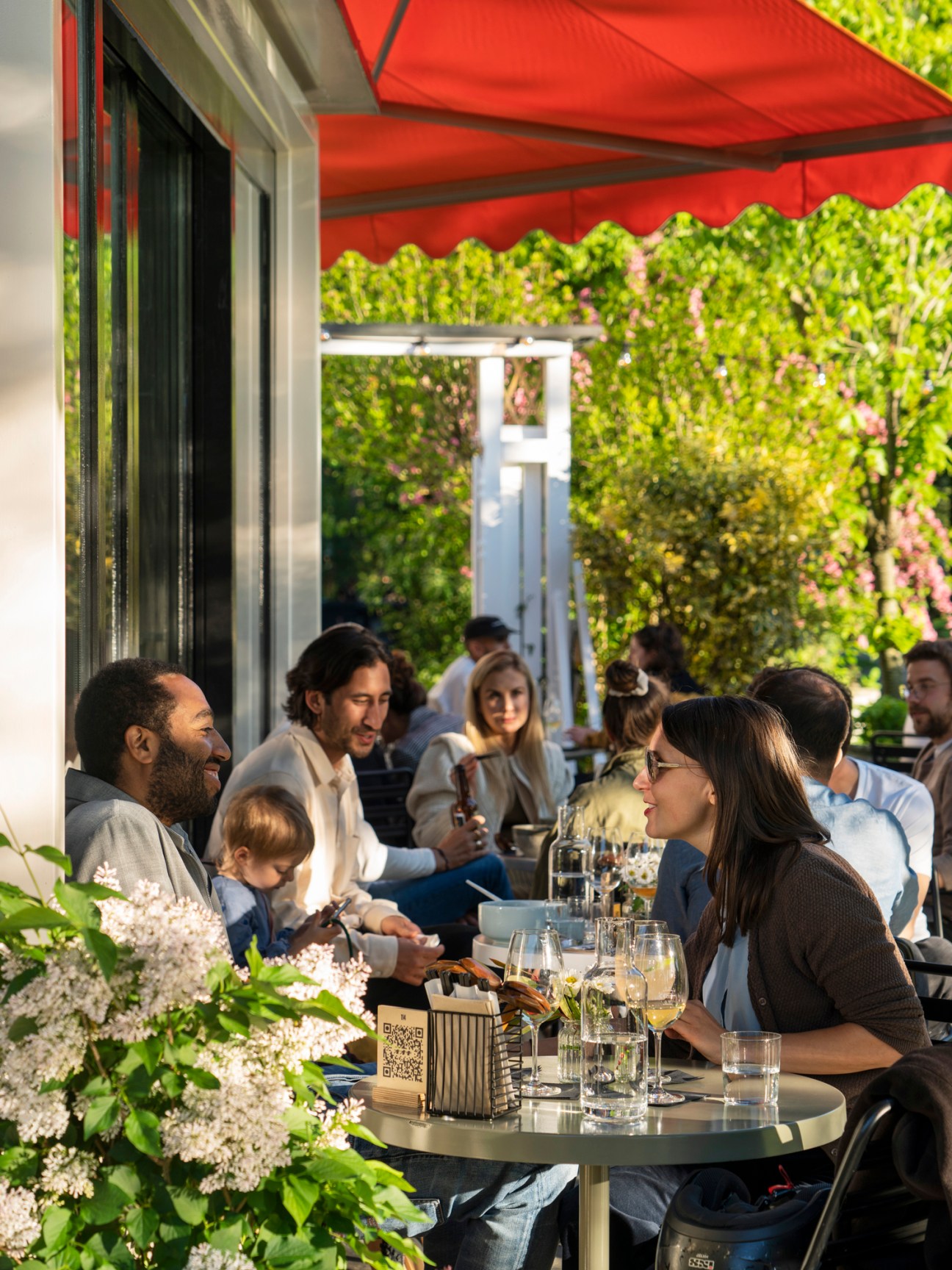 Diners enjoying dinner on the terrace of Ooki Pavilion under red awnings with lush green foliage.