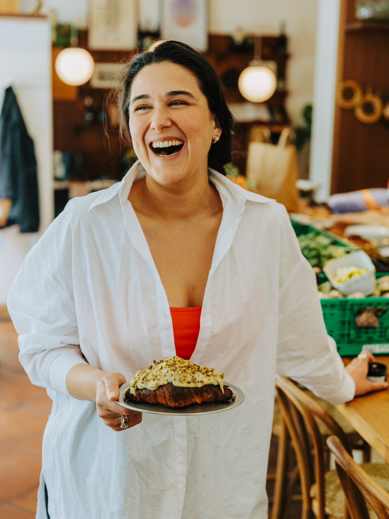 Woman laughing while holding a frosted cake in a bakery kitchen