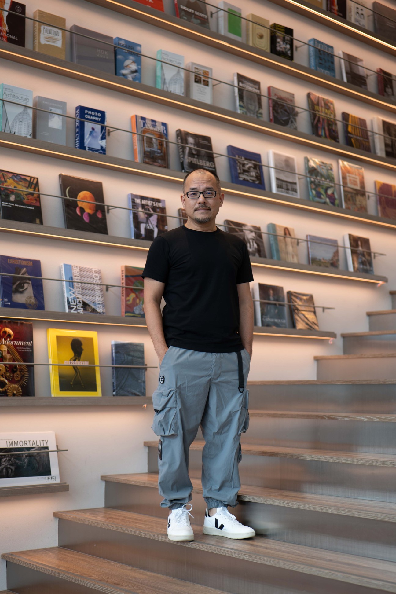 Man standing in front of illuminated shelving displaying books and magazines in a retail space.