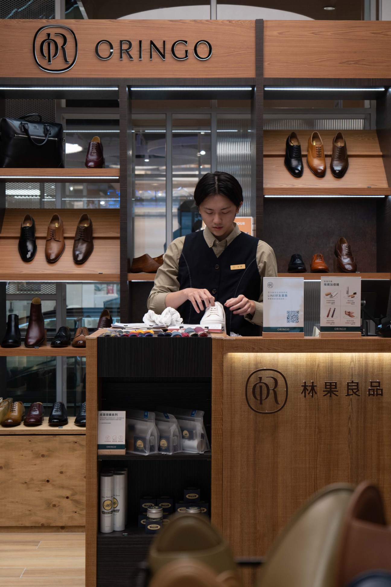 A sales associate at a wooden counter inside a Cringo shoe retail store displaying leather footwear.