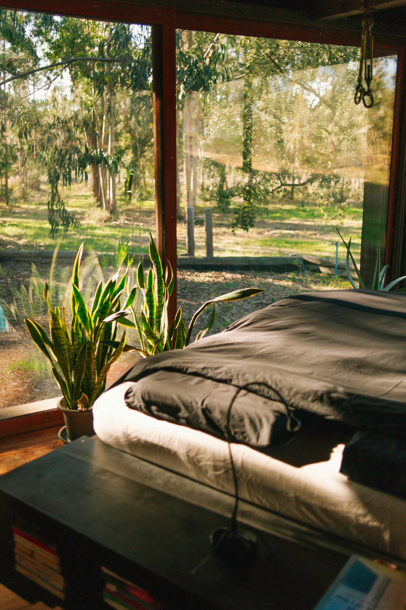 Unmade bed with gray bedding next to large windows overlooking trees and countryside