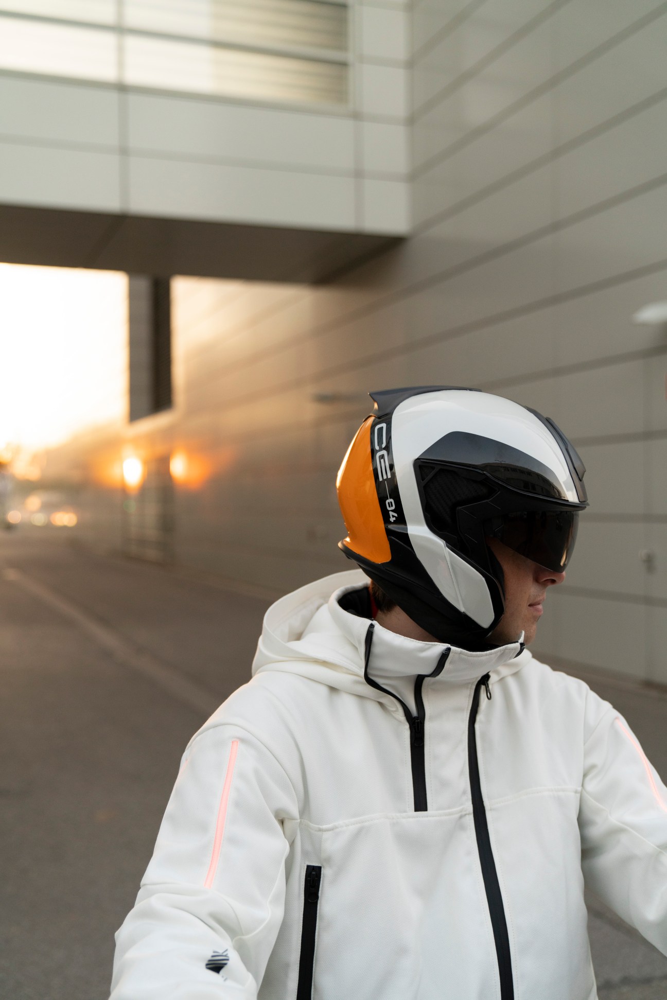 Person wearing a white and orange helmet and white jacket in a modern urban setting.