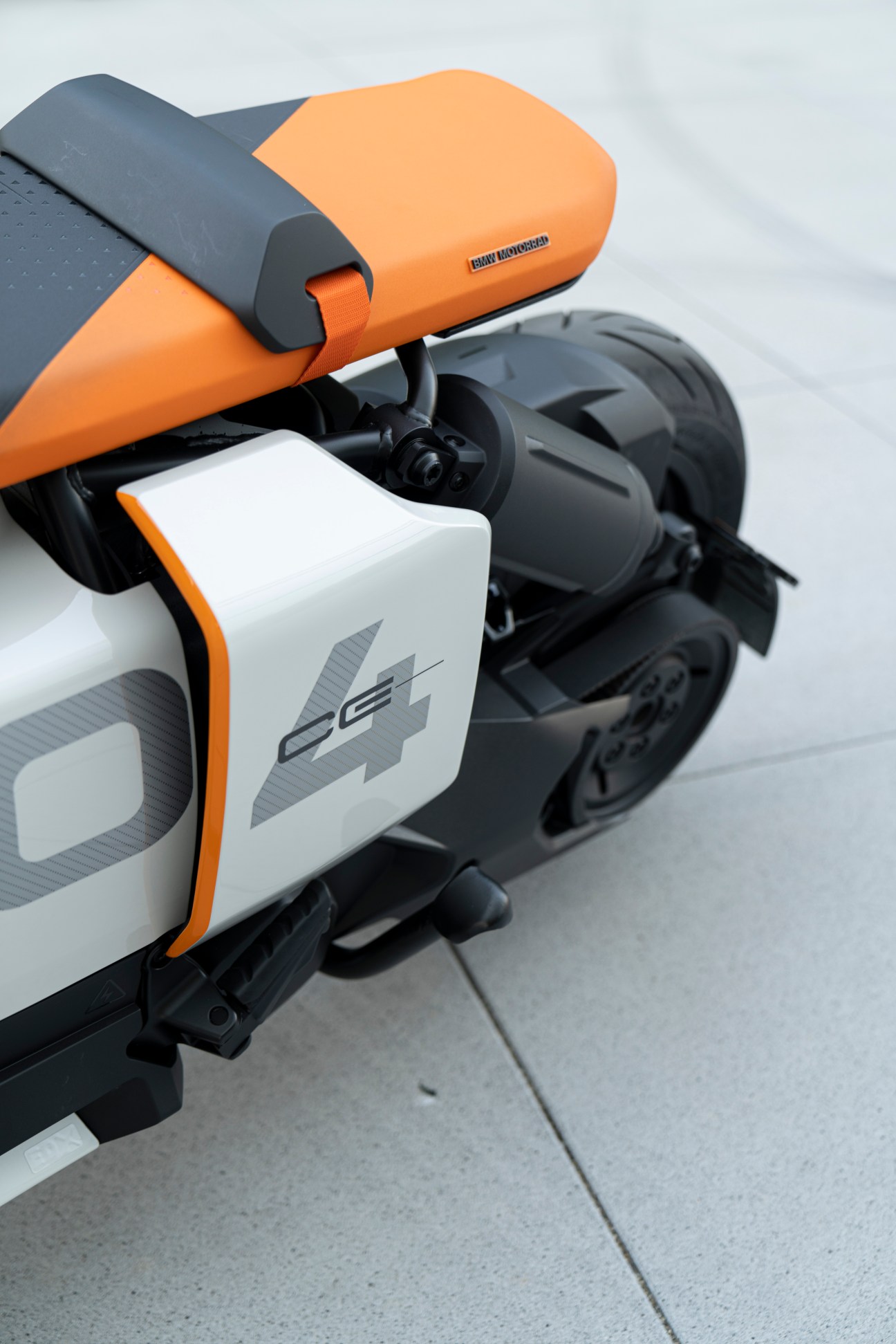 Close-up detail of the BMW Definition Motorrad CE 04 electric scooter showing orange seat and white body panel with CE 04 branding.