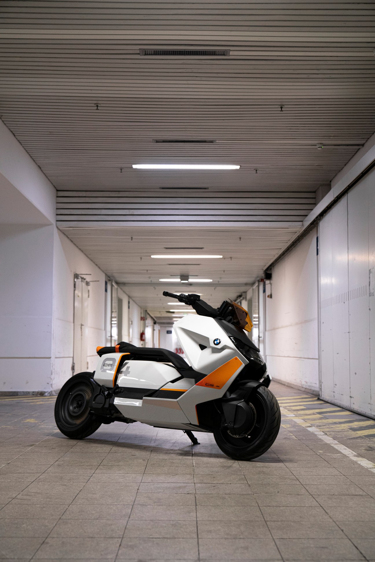 BMW Definition Motorrad CE 04 electric scooter in white and orange parked in a modern corridor.