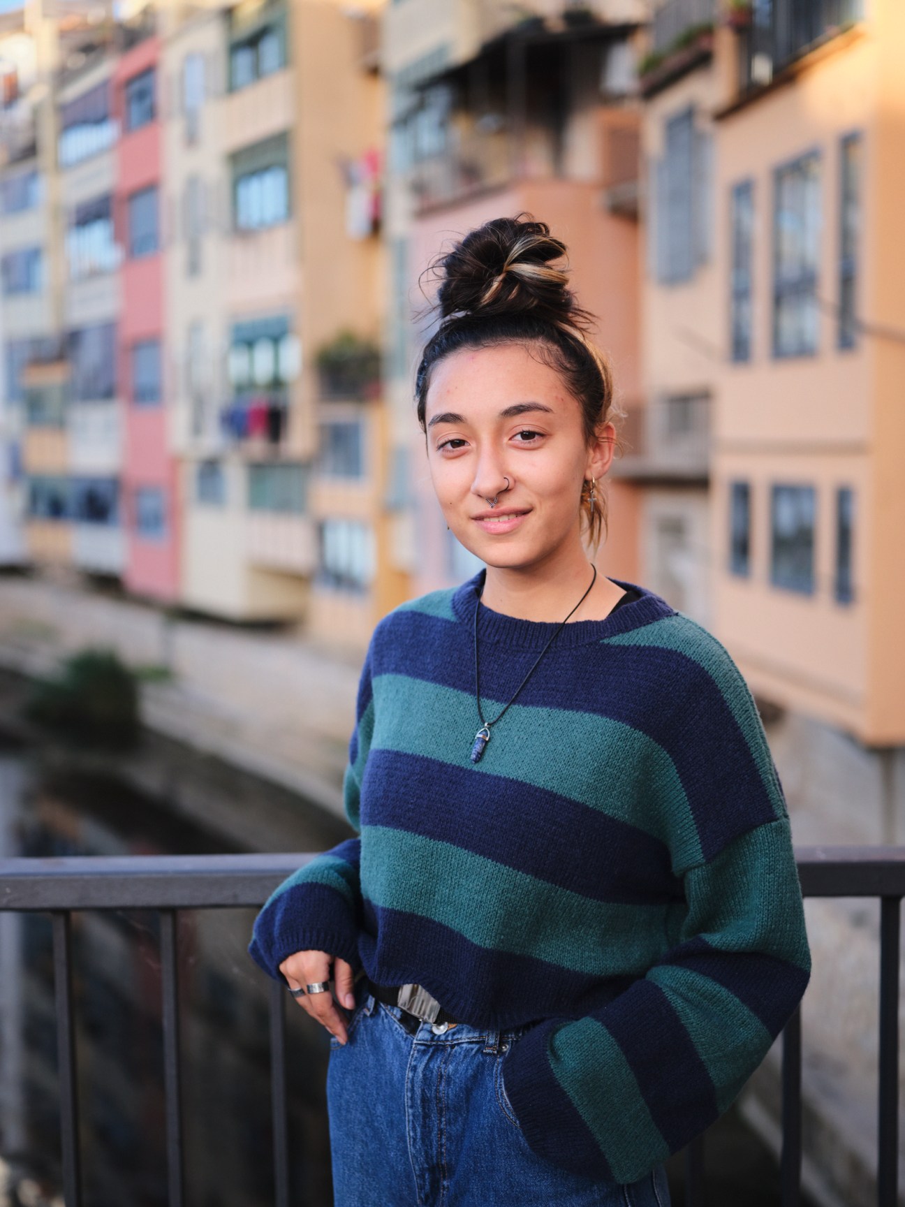 Woman in striped sweater standing on balcony with colorful buildings behind her in Girona.
