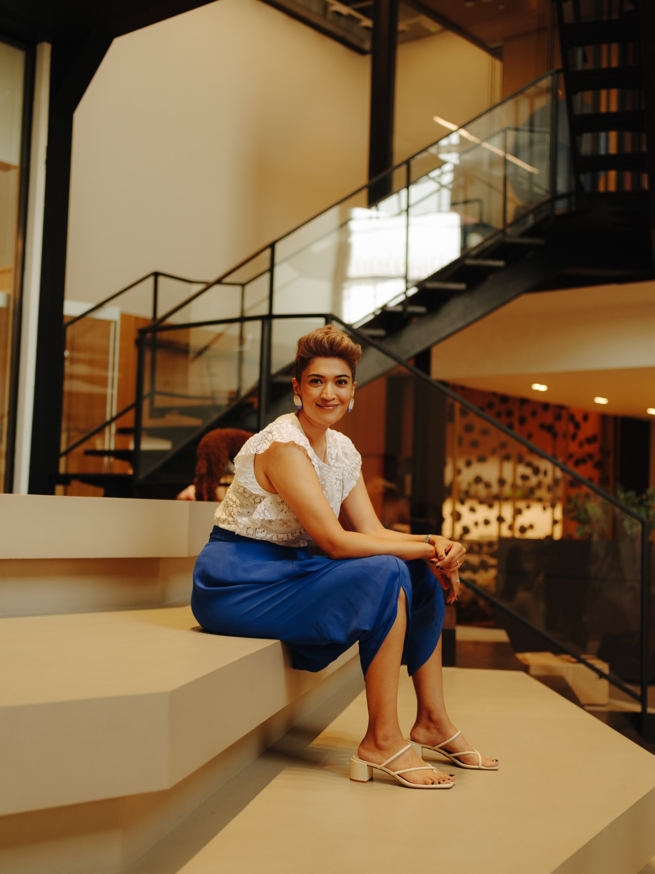 Pallavi Dean, founder of design studio Roar, poses on a modern staircase in a contemporary interior space.