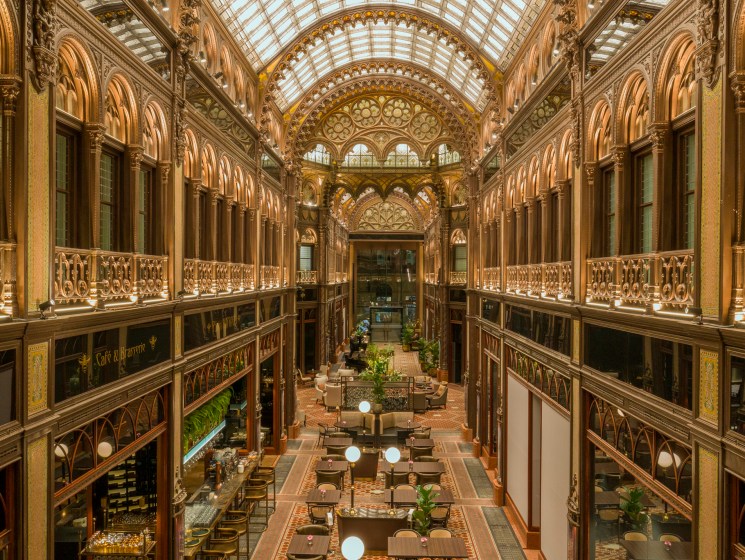 Ornate grand hotel atrium with gilded balconies and glass ceiling.