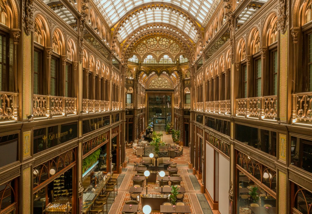 Ornate glass-roofed arcade with dining tables and decorative ironwork at Parisi Udvar hotel in Budapest