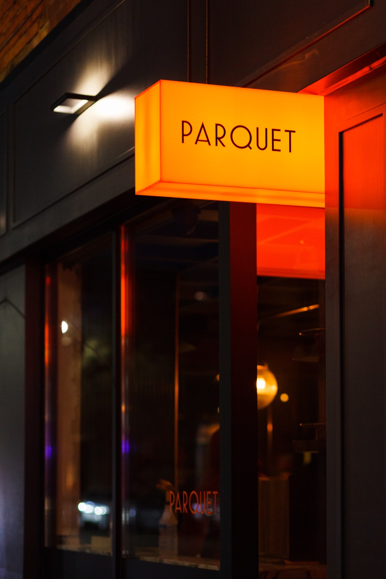 Illuminated orange sign reading 'PARQUET' hanging outside a restaurant storefront at night
