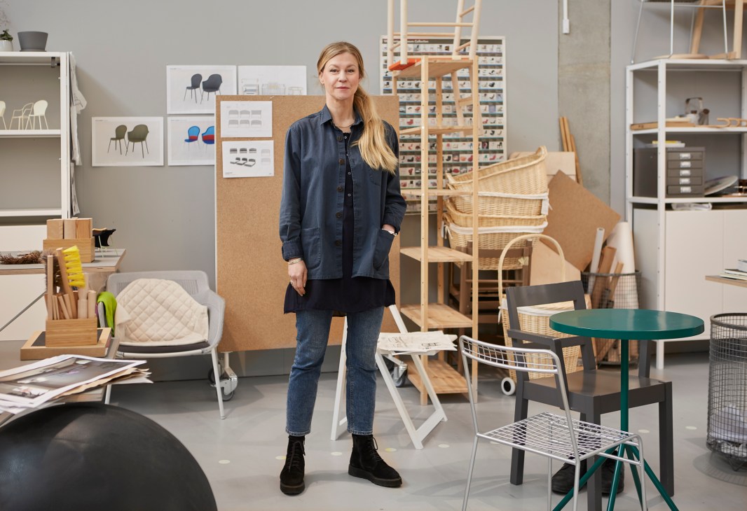 Woman in denim jacket standing in design studio surrounded by furniture prototypes and design materials