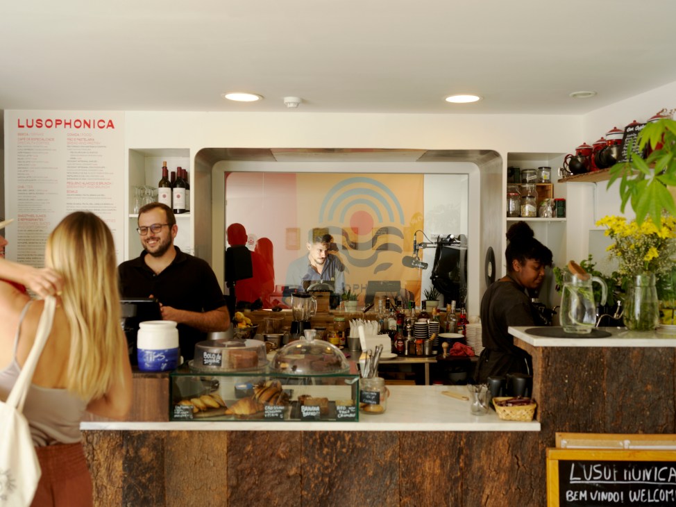 Interior of Lusophonica cafe with counter staff serving customers, featuring modern design with plants and geometric wall art
