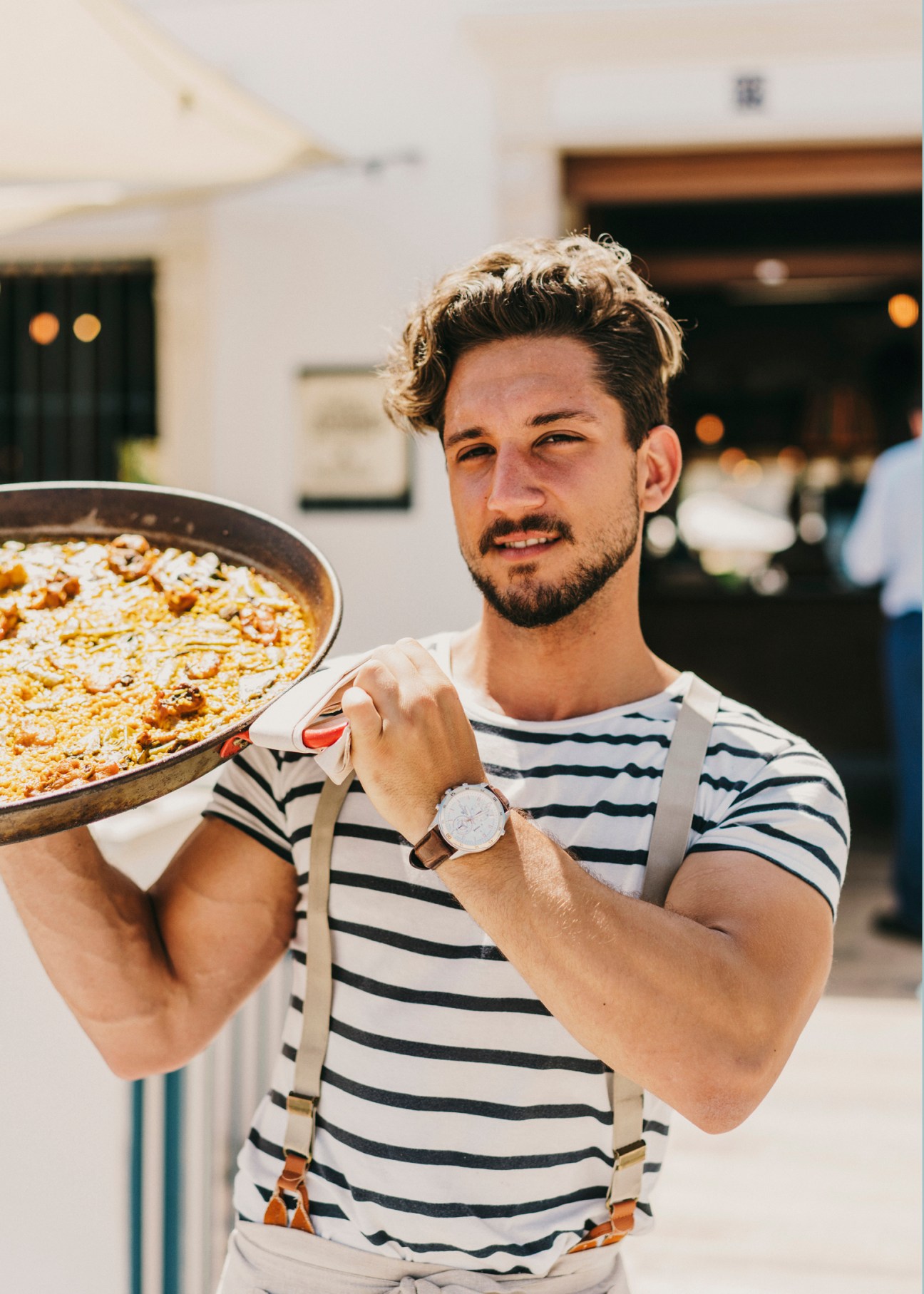 Man holding a paella pan at Platja de la Patacona beach in Valencia, Spain.