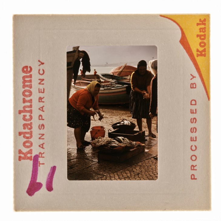 A vintage Kodak slide showing fishermen working with nets and boats on a cobblestone waterfront
