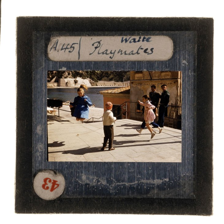Vintage slide photo showing children and adults playing in a sunny Mediterranean courtyard, labeled 'Walk Playmates'