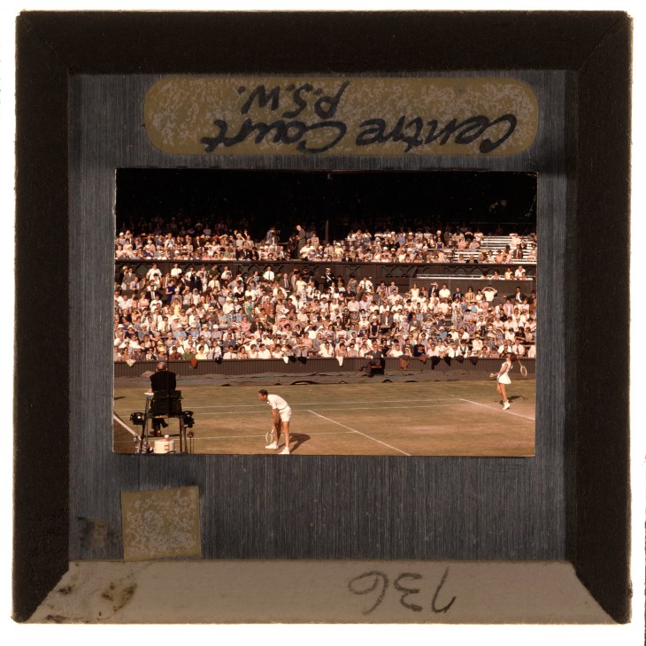 Vintage photograph showing tennis match in progress with crowded stadium stands and umpire's chair visible