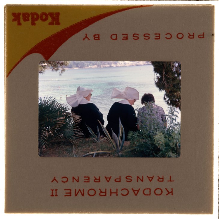 Kodak film slide showing three people in head coverings sitting by water with palm trees visible