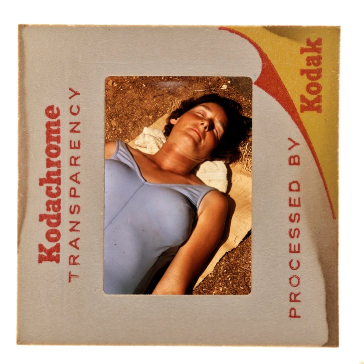 A vintage Kodak slide mount containing a photograph of a person lying on straw or dried grass in sunlight