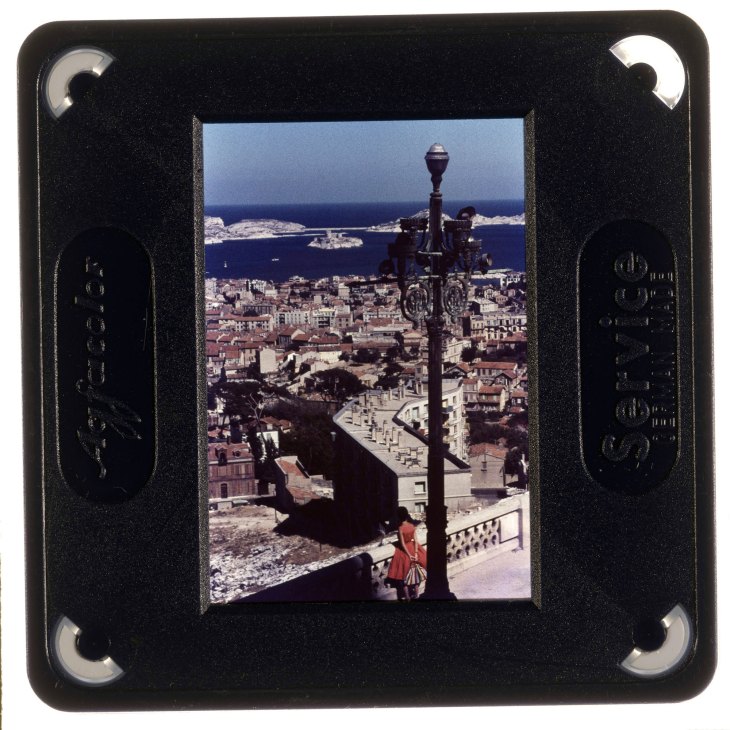 Vintage color slide showing Mediterranean coastal town with ornate lamp post in foreground and blue sea beyond
