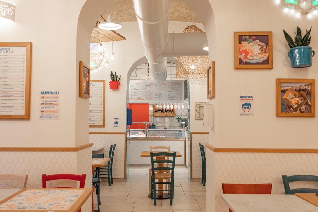 Interior of Pescaria fish-focused street food outlet in Rome's Prati neighbourhood with counter, seating and menu boards.
