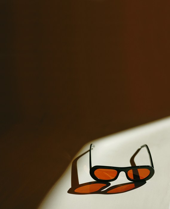 Orange-tinted sunglasses casting shadow on white surface in warm lighting