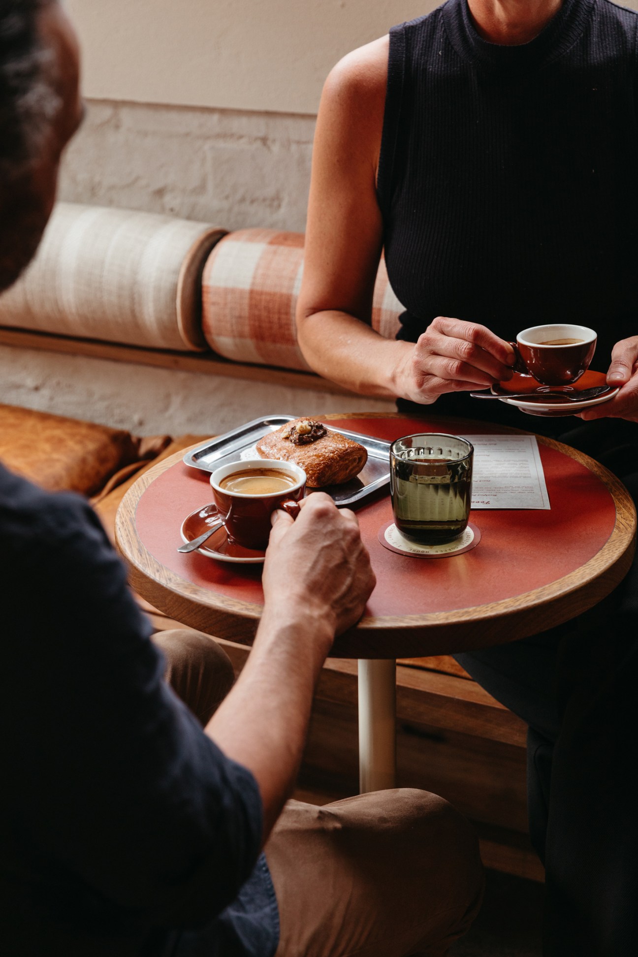 Two people enjoying coffee and pastry at Genovese Coffee House with terracotta interior