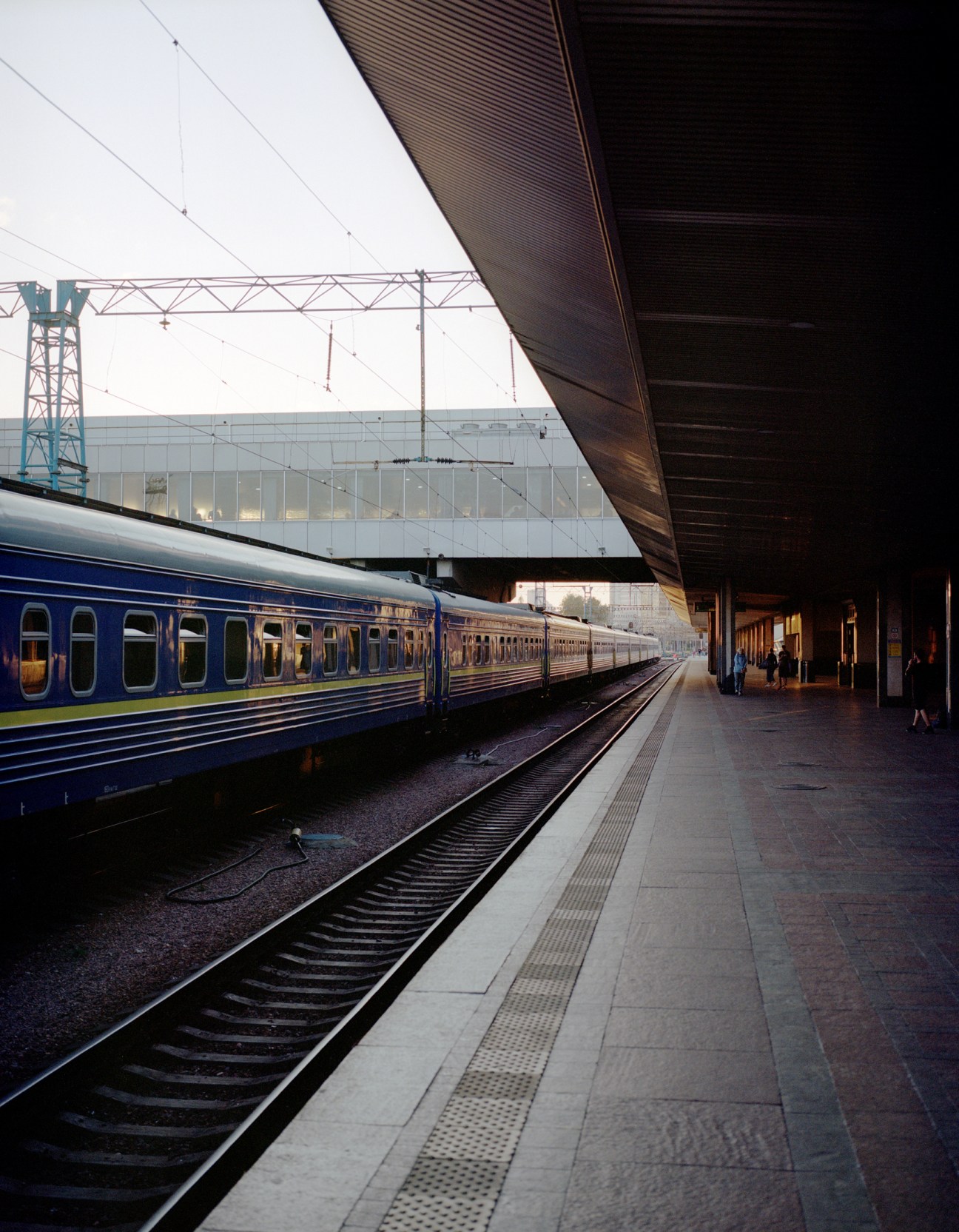 Blue and yellow passenger train arriving at covered railway platform in early morning light
