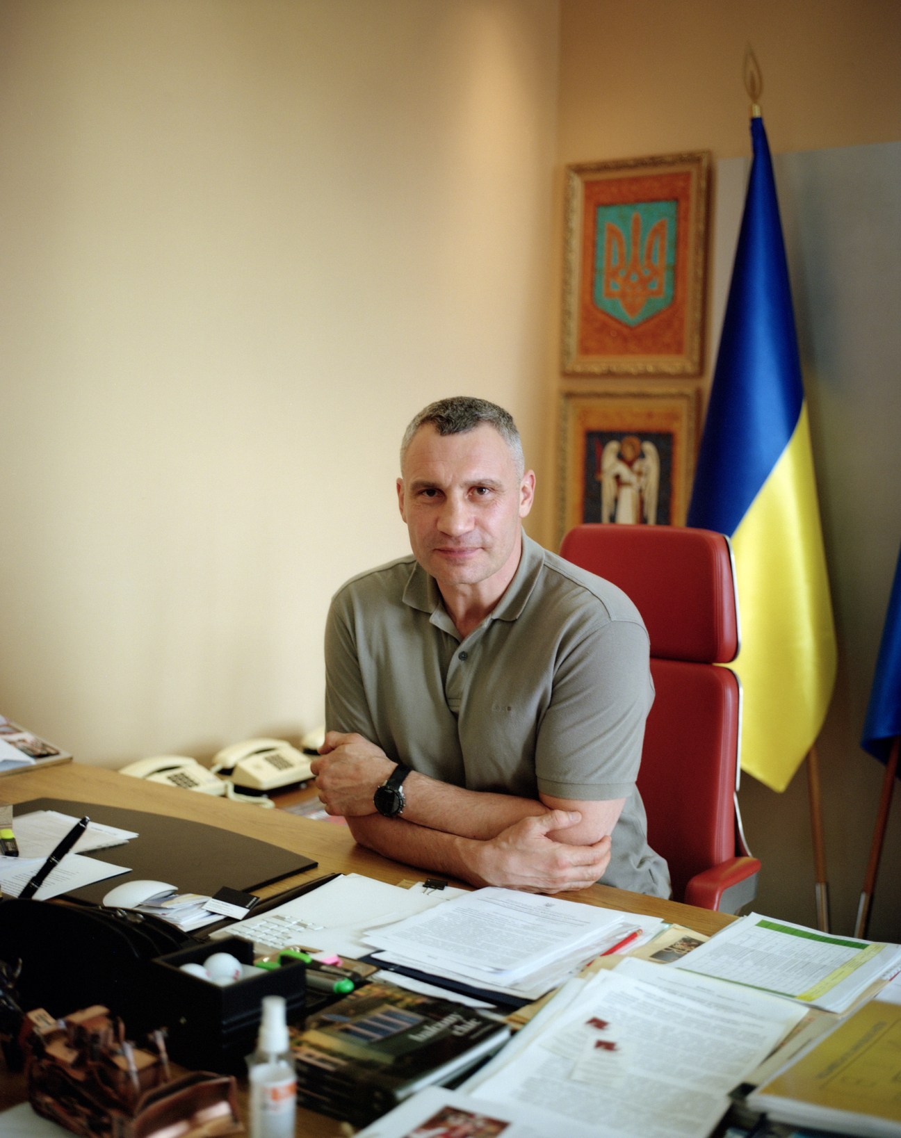 Vitali Klitschko sitting at his desk in his office with Ukrainian flag and coat of arms behind him