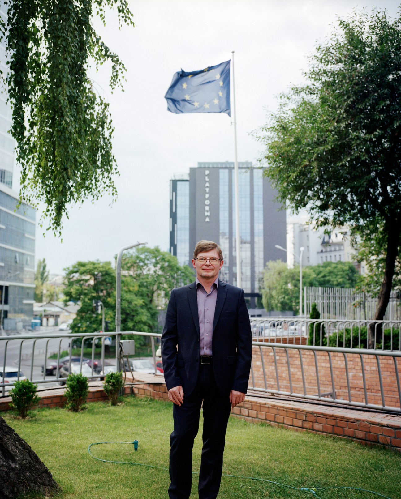 Man in dark suit standing outdoors with European Union flag in background
