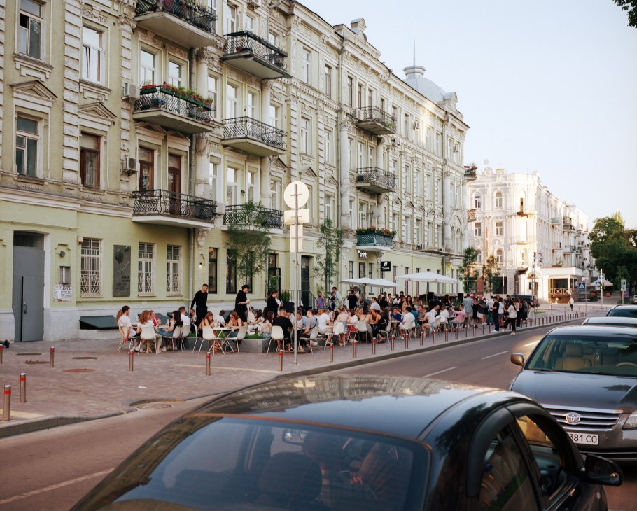 People dining at outdoor restaurant tables along a historic street in Kyiv's Zoloti Vorota district at evening