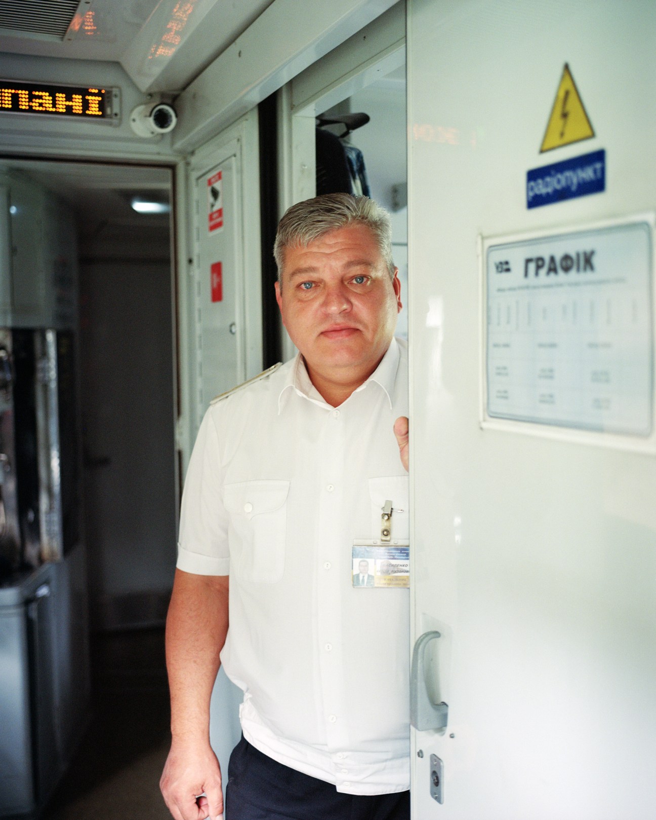 Train director Serhii Viktorovych wearing a white polo shirt and ID badge standing in a train corridor