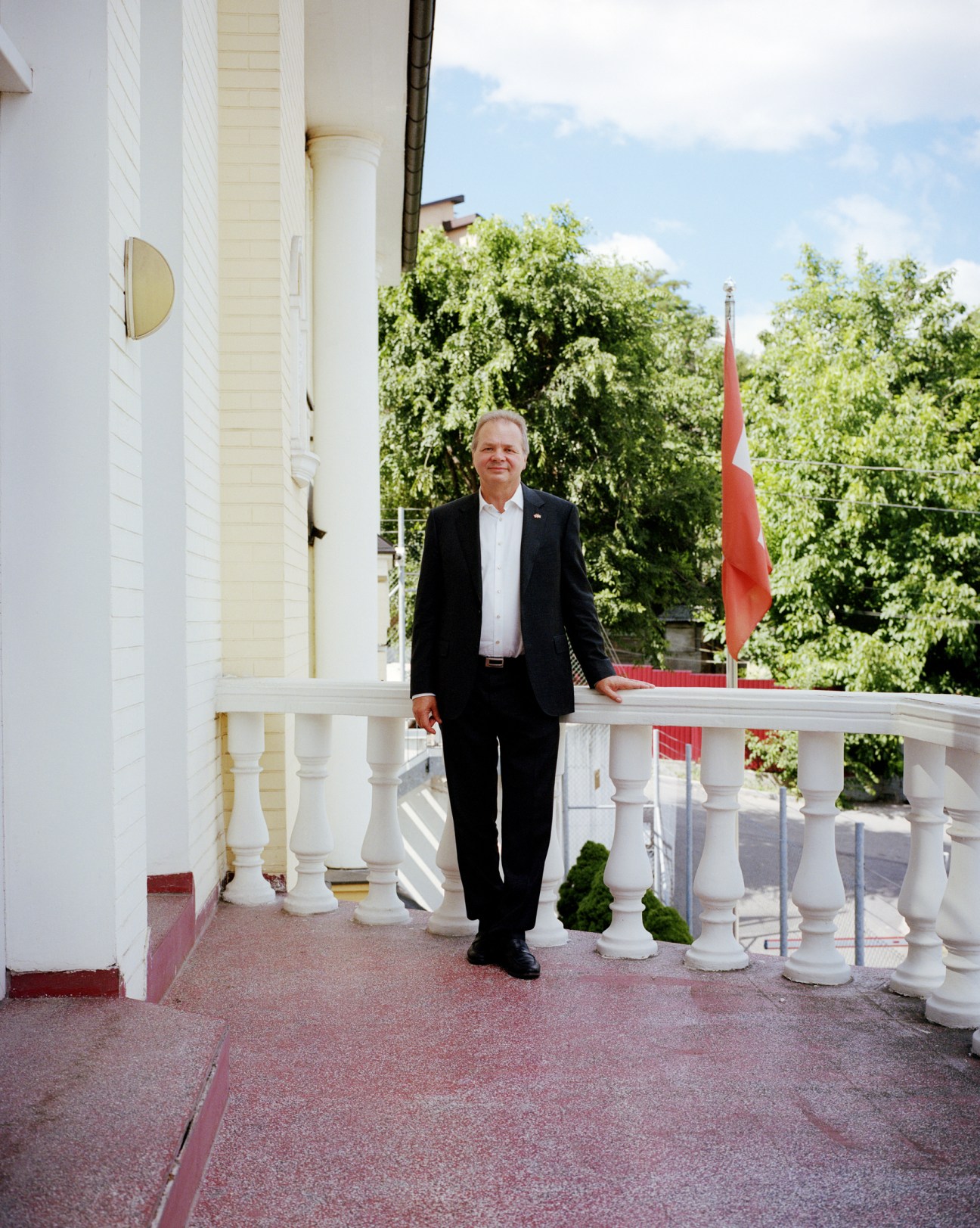 Swiss Ambassador to Ukraine Claude Wild standing on a white balcony with columns and a red flag