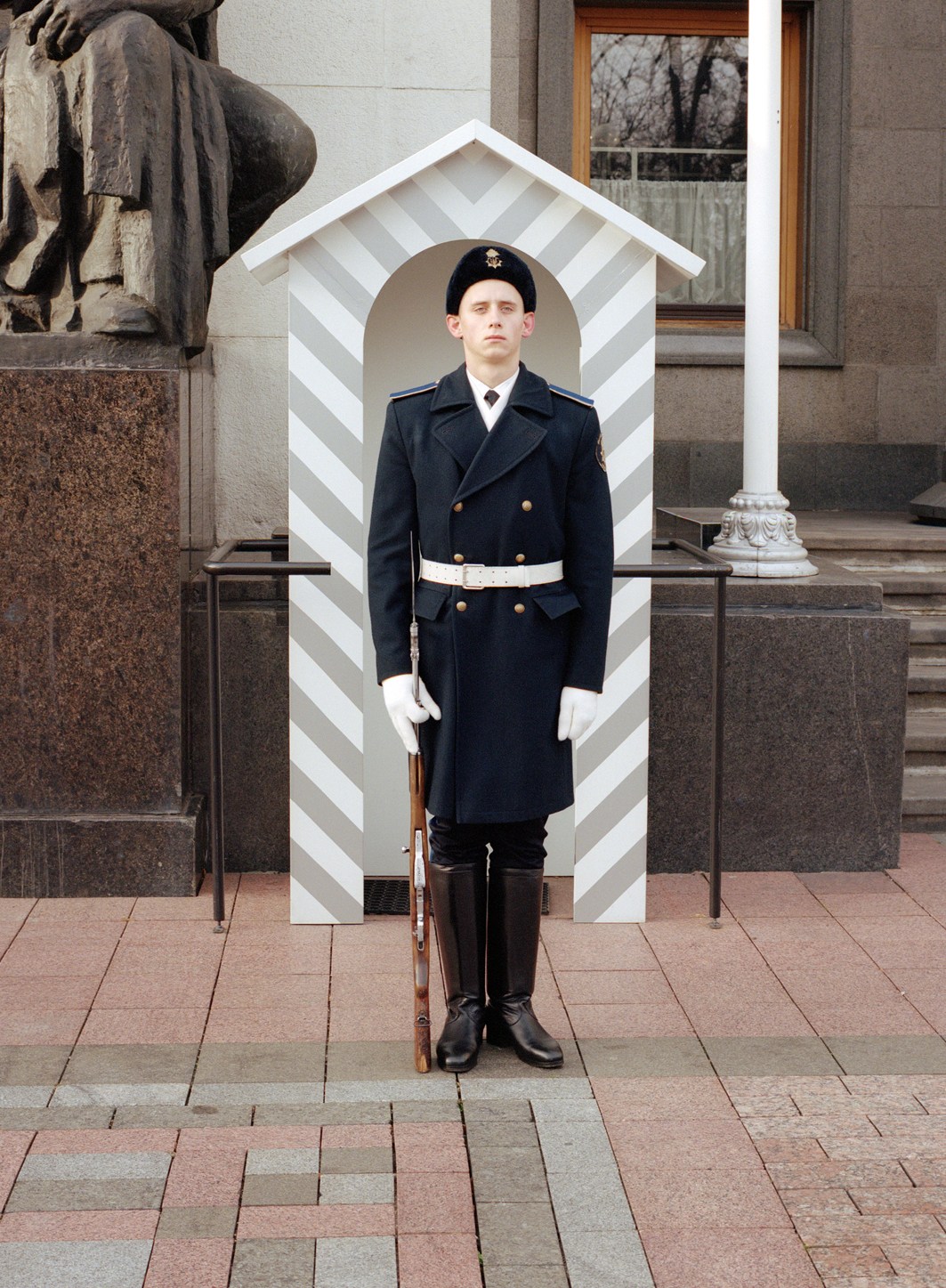Guard in dark blue military uniform standing at attention in white striped sentry box