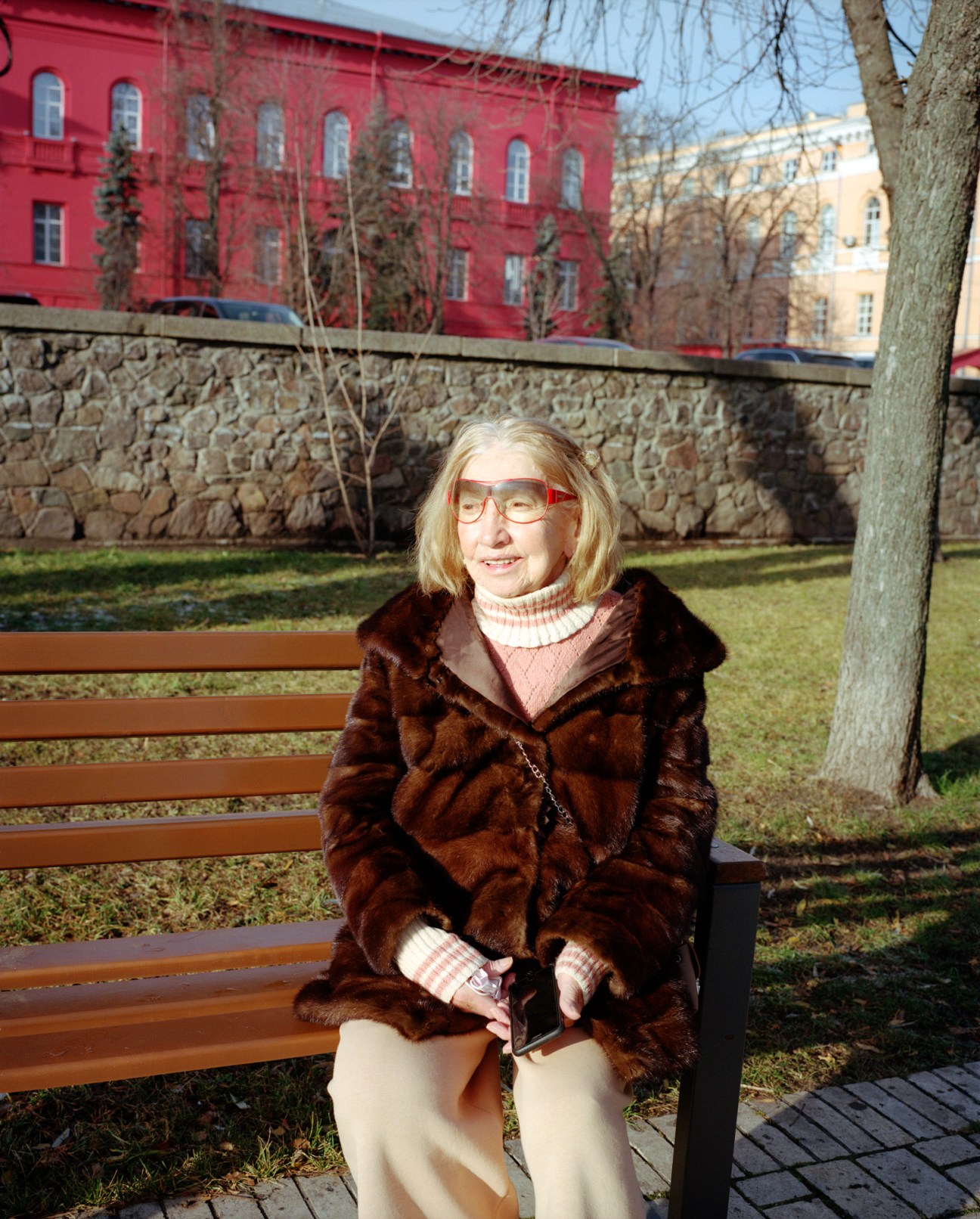 Woman in brown fur coat sitting on park bench in winter