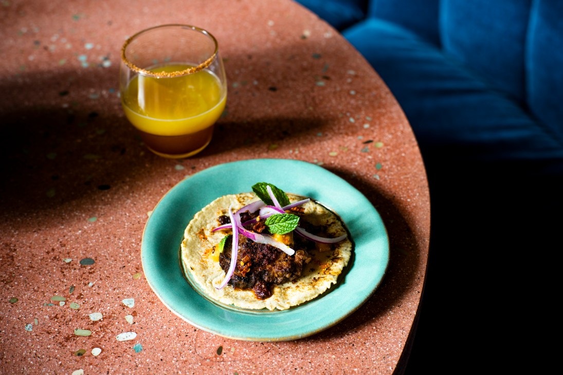 Braised lamb taco garnished with purple onions and mint on a turquoise plate with yellow cocktail
