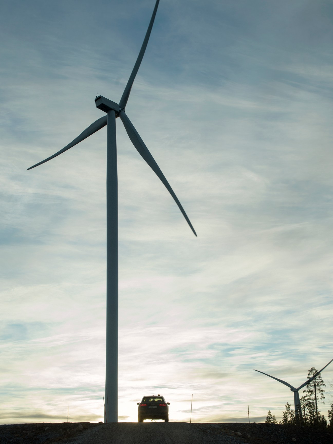Wind turbine with three blades against cloudy sky and car on road below in northern Sweden