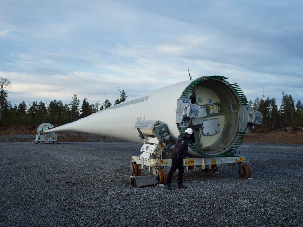 Worker in safety gear examining large white wind turbine blade