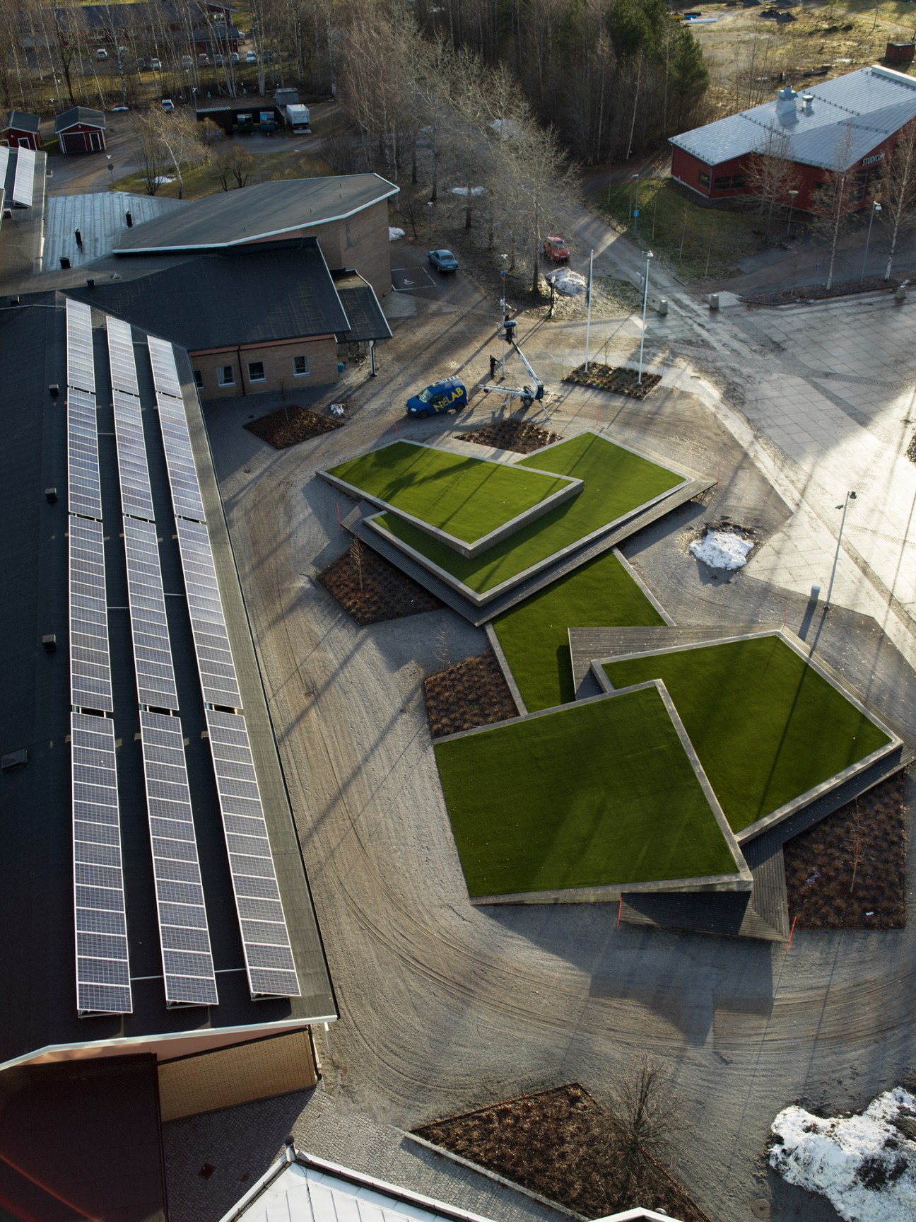 Aerial view of solar panels on industrial building roof with geometric green grass landscaping and forest backdrop