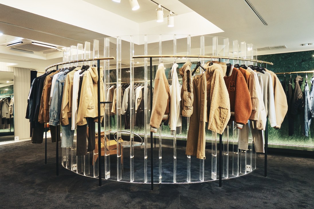 Circular glass clothing rack displaying neutral-toned jackets and coats in modern retail space